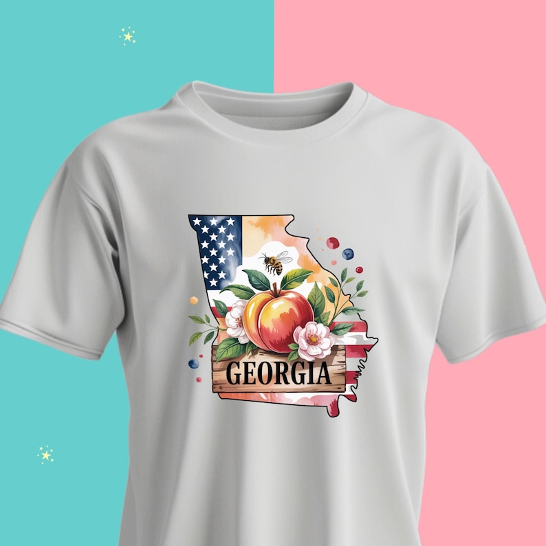 May include: White t-shirt featuring a colorful graphic of the state of Georgia. The design includes a peach, flowers, a bee, and the text "GEORGIA" on a wooden sign. The background incorporates the American flag.