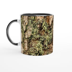 May include: A white ceramic mug with a black rim and handle. The mug features a close-up image of tree bark with green moss growing on it.