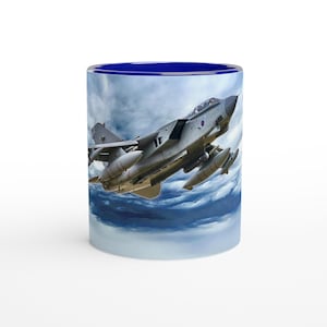 Puede incluir: Una taza de cerámica azul y blanca con una foto de un avión de combate gris volando a través de las nubes. El avión tiene un círculo rojo, blanco y azul en el lateral.