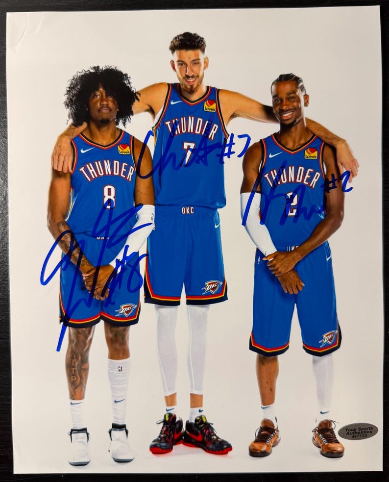 Puede incluir: Fotograf&iacute;a de tres jugadores de baloncesto con camisetas azules y naranjas de los Thunder. Cada camiseta tiene un n&uacute;mero y la palabra "Thunder". Los jugadores est&aacute;n de pie juntos, con un jugador abrazando a los otros dos. La foto est&aacute; firmada con tinta azul.