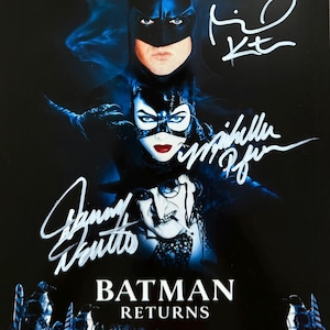 May include: A Batman Returns movie poster featuring Batman, Catwoman, and the Penguin with white ink signatures from Michael Keaton, Michelle Pfeiffer, and Danny DeVito. The dark blue and black poster includes the film title and cast credits.