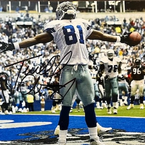 May include: A signed photograph of a football player in a white and blue uniform, number 81, holding a football. The player is in a stadium with a crowd in the background. The photograph is signed in black ink.