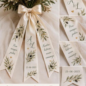 May include: A cream-coloured satin ribbon tied in a bow around a floral bouquet, featuring hand-painted olive branches, small gold hearts, and the text A & L, Para siempre juntos, Nuestra historia recién comienza, and the date 15-06-2025.