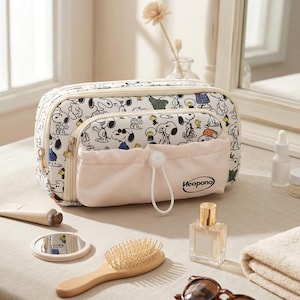 May include: A rectangular white toiletry bag featuring a repeating Snoopy and Woodstock print. The bag has a front pocket with a light pink drawstring closure and the text "Heopono" printed in black. It includes two zippered compartments.