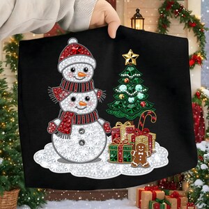 Könnte beinhalten: Ein schwarzes, weihnachtliches Dekokissen mit einem Schneemann mit roter Mütze und Schal, einem grünen Weihnachtsbaum, verpackten Geschenken und einem Lebkuchenmann. Der Schneemann hat ein funkelndes Design.