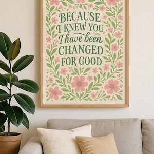May include: A framed print with the text "BECAUSE I KNEW YOU, I HAVE BEEN CHANGED FOR GOOD" in green script. The text is surrounded by pink flowers and green leaves. The frame is light brown.