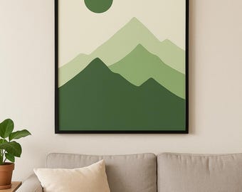May include: A framed art print featuring a minimalist mountain landscape in shades of green. A dark green circle represents the sun. The artwork is in a black frame, displayed above a gray sofa with a beige pillow.