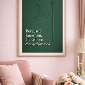 Könnte beinhalten: Gerahmter Kunstdruck mit dunkelgrünem Hintergrund, geprägten Illustrationen eines Zauberhuts und eines Zauberstabs. Der Text "Because I knew you, I have been changed for good" ist in Weiß und Rosa gedruckt.