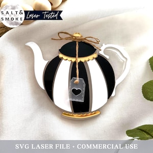 Può includere: Teiera a strisce bianche e nere con un bordo dorato e un piccolo cartellino a forma di cuore appeso. La teiera è su una superficie bianca.