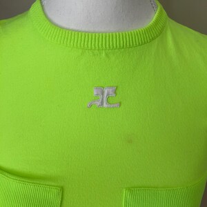 Puede incluir: Una camiseta de color verde ne&oacute;n brillante con un logotipo blanco de las letras "RC" en la parte delantera. La camiseta tiene una textura acanalada y un bolsillo en la parte inferior.