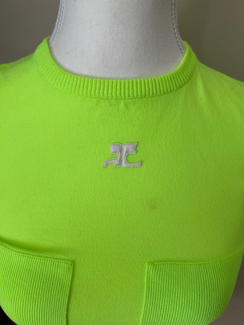 Puede incluir: Una camiseta de color verde ne&oacute;n brillante con un logotipo blanco de las letras "RC" en la parte delantera. La camiseta tiene una textura acanalada y un bolsillo en la parte inferior.