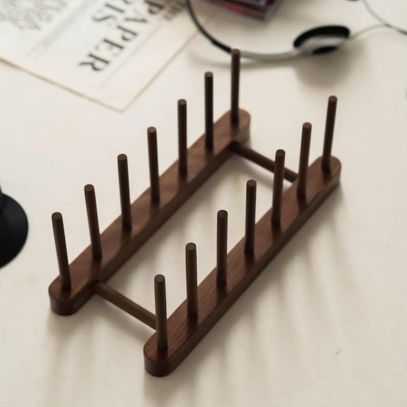 May include: A wooden plate rack with a dark brown finish. The rack has a rectangular shape with multiple vertical pegs designed to hold plates. The design is simple and functional, suitable for kitchen organization.