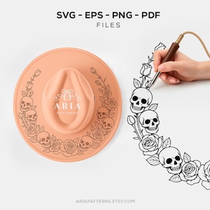 May include: A peach-colored hat with a decorative skull and rose design. The hat features the text "ARIA PATTERNS" and the words "SVG - EPS - PNG - PDF FILES". The design is being drawn with a wood-handled tool.