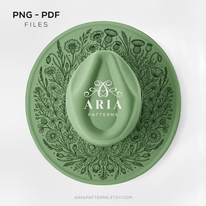 May include: A sage green fedora hat featuring a dark green botanical illustration of wildflowers and thistles around the crown. The center of the hat displays the white text ARIA PATTERNS with a decorative swirl logo above the brand name.