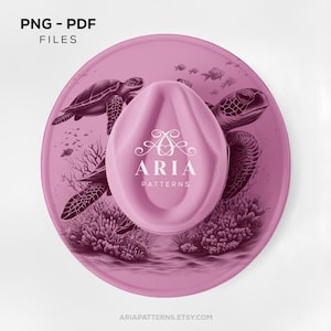 May include: A pink cowboy hat with a sea turtle design. The hat features a light pink crown and a wide brim with an illustration of two sea turtles, coral, and fish. The text "ARIA PATTERNS" is printed on the crown.