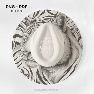 Può includere: Un cappello fedora bianco con una corona color crema e un'ampia tesa con una dettagliata illustrazione di tigre in bianco e nero. Il cappello ha il testo "ARIA PATTERNS" stampato sulla corona. L'immagine include anche il testo "PNG - PDF FILES".