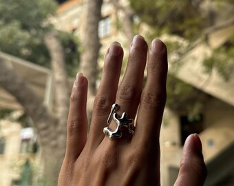 May include: A silver ring with an abstract, organic design. The ring is worn on the index finger of a hand.