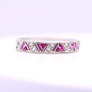 Könnte beinhalten: Ein silberfarbener Bandring mit einem sich wiederholenden Muster aus dreieckig geschliffenen rosa Steinen, die sich mit kleinen, runden, klaren weißen Steinen abwechseln, welche in das Metallband eingefasst sind und ein durchgehendes Design bilden.