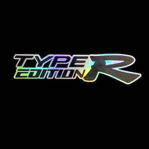May include: A holographic sticker with the words "TYPE EDITION R" in a stylized font. The text has a gradient effect with colors like green, blue, and yellow, set against a black background.