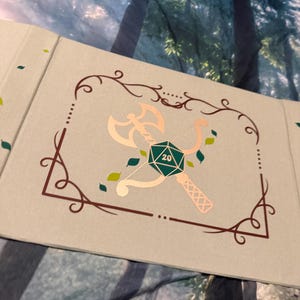 May include: A light gray book cover featuring a dark brown decorative border. In the center, a metallic copper illustration shows a battle axe crossed with a bow, centered behind a green twenty-sided die with the number 20 printed in white.