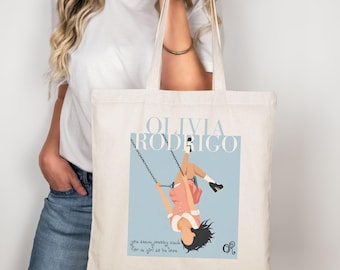 Może przedstawiać: Kremowa torba typu tote z grafiką przedstawiającą osobę na huśtawce, z napisem "OLIVIA RODRIGO" w jasnoniebieskim kolorze. Torba zawiera również tekst "you know pretty sounds for a girl as in love."