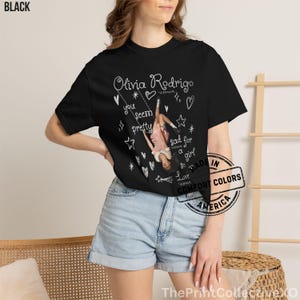 May include: Black t-shirt featuring a graphic of Olivia Rodrigo on a swing, with the text "Olivia Rodrigo" and song lyrics. The design includes hearts, stars, and the words "you seem pretty" and "sad for a girl".