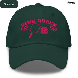 May include: Spruce green baseball cap with the text "DINK QUEEN" embroidered in pink, along with a pickleball paddle, ball, and bows. The cap has a curved brim and a structured crown.