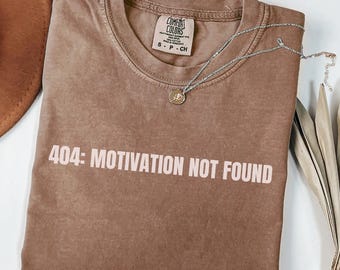 May include: A brown t-shirt with the text "404: MOTIVATION NOT FOUND" printed in white. The shirt is made by Comfort Colors and the color is Espresso.