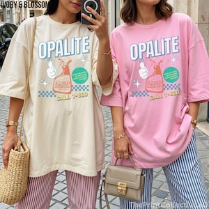 May include: Two oversized t-shirts, one cream and one pink, each with the word "OPALITE" in large letters. The shirts feature a graphic of a spray bottle and the text "CALL 1-800". The shirts are paired with striped pants.