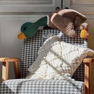 May include: A crocheted duck plush toy with brown and green yarn, sitting on a black and white checkered armchair with a white crocheted pillow.