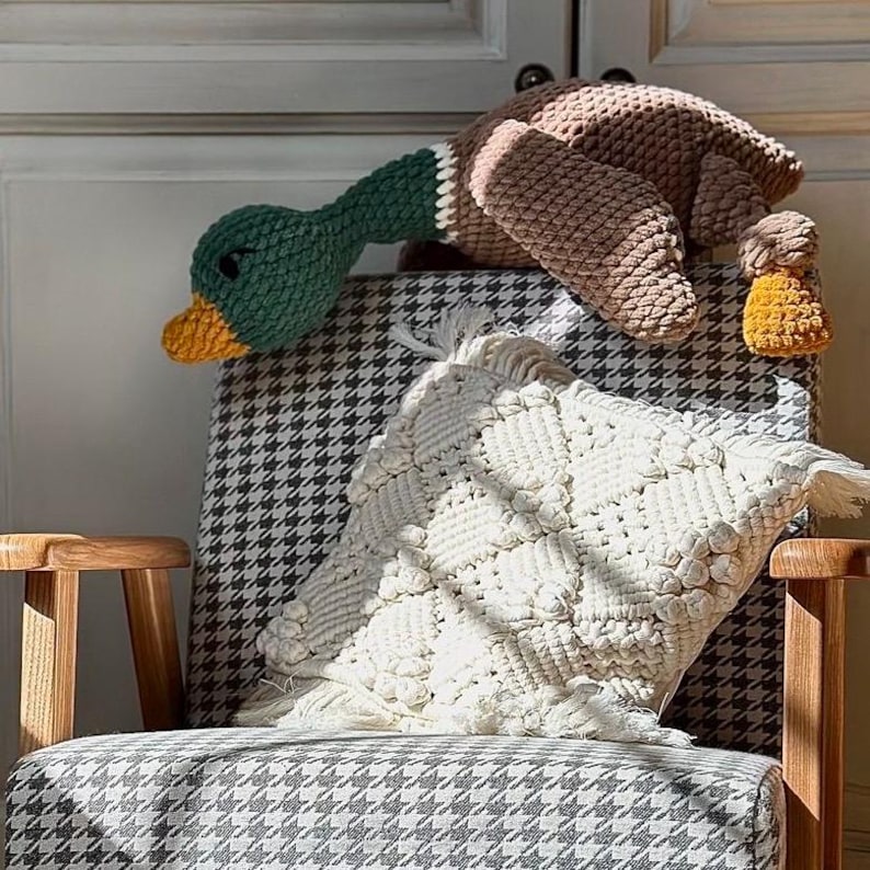 May include: A crocheted duck plush toy with brown and green yarn, sitting on a black and white checkered armchair with a white crocheted pillow.