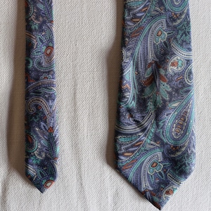 May include: A patterned necktie with a paisley design in shades of blue, teal, and orange. The tie is made of a soft fabric and is suitable for formal or business attire. The tie is approximately 58 inches long.