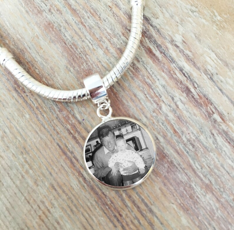 May include: A silver charm bracelet with a round photo charm featuring a black and white photo of a man holding a young child.