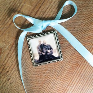 May include: A silver picture frame with a black and white photo of a couple. The frame is tied with a light blue ribbon.