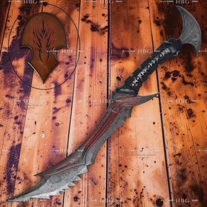 May include: A fantasy-style dagger with a curved blade and a serrated edge. The handle is wrapped in black material with silver accents. A wooden plaque with a stylized design is visible in the background.