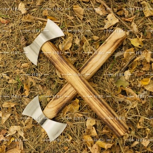 May include: Two wooden-handled throwing axes with double-headed blades, crossed against a background of dry leaves and grass.