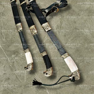 K&ouml;nnte beinhalten: Drei verzierte Schwerter mit schwarzen Ledergriffen und goldenen Akzenten. Die Klingen sind mit komplizierten Mustern verziert und die Griffe sind mit wei&szlig;en und schwarzen knochenartigen Materialien verziert.
