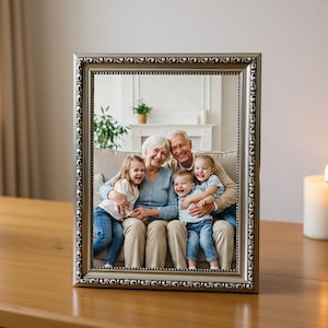 May include: A silver framed photograph displays a family portrait. The photo shows two older adults seated with three young children. The frame is on a wooden table, with a lit candle and potted plants nearby.