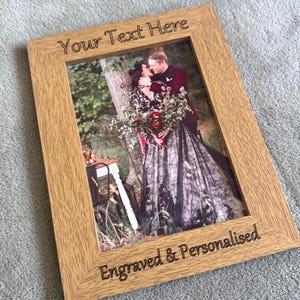 May include: A light oak picture frame with the text "Your Text Here" and "Engraved & Personalised". The frame contains a photo of a couple. The woman wears a black lace dress and holds a bouquet of flowers.