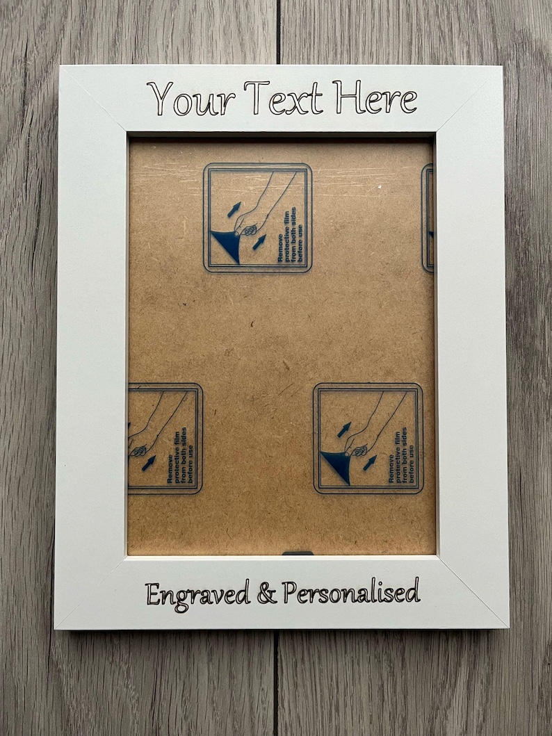 Op de afbeelding: Een witte fotolijst met de tekst "Your Text Here" bovenaan en "Engraved & Personalised" onderaan. De lijst heeft een rechthoekige opening en bevat instructies om de beschermfolie te verwijderen.