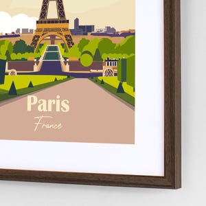Puede incluir: Una impresión artística enmarcada que presenta una ilustración estilizada de París, Francia. La obra de arte muestra la Torre Eiffel, árboles verdes y un camino. Las palabras "Paris France" se muestran en una fuente vintage.