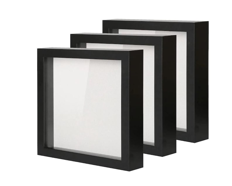 May include: Three black shadow box frames with white interiors. The frames are square and have a deep profile, creating a three-dimensional effect. Suitable for displaying artwork or collectibles. Each frame is approximately 20 cm square.