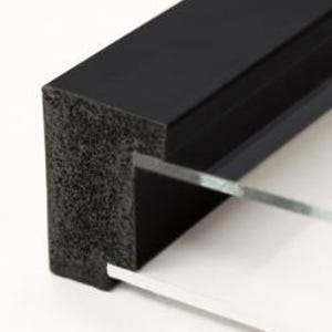 May include: Close-up of a black picture frame with a textured, foam-like edge. Clear glass and a white backing are visible. The frame is designed to hold a photograph or artwork, suitable for display.