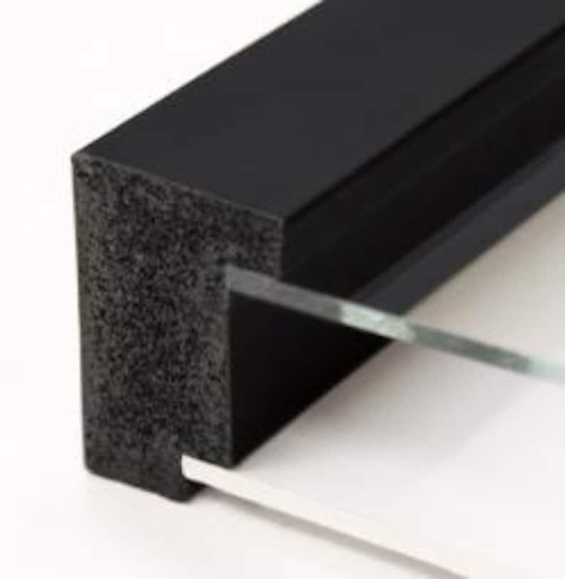 May include: Close-up of a black picture frame with a textured, foam-like edge. Clear glass and a white backing are visible. The frame is designed to hold a photograph or artwork, suitable for display.