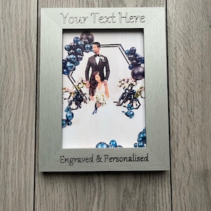 Op de afbeelding: Zilveren rechthoekige fotolijst met de tekst "Your Text Here" bovenaan en "Engraved & Personalised" onderaan. De lijst bevat een trouwfoto met een stel en ballondecoraties.