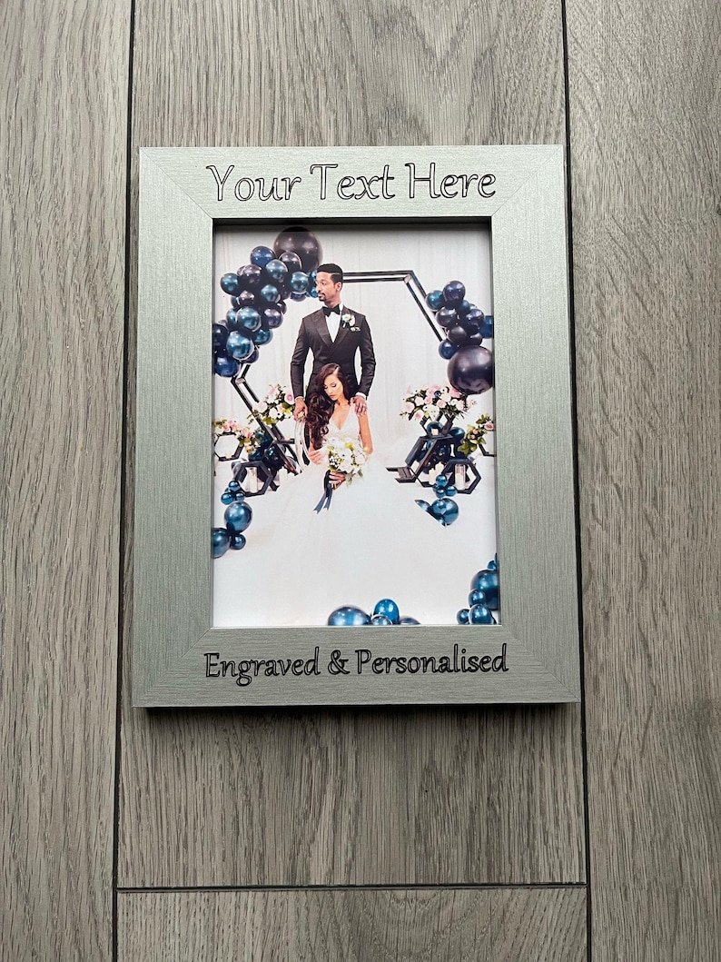 Op de afbeelding: Zilveren rechthoekige fotolijst met de tekst "Your Text Here" bovenaan en "Engraved & Personalised" onderaan. De lijst bevat een trouwfoto met een stel en ballondecoraties.