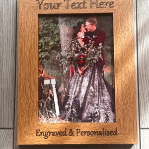 Op de afbeelding: Een rechthoekige houten fotolijst met de gegraveerde tekst "Your Text Here" en "Engraved & Personalised". De lijst bevat een foto van een knuffelend stel. De lijst is gemaakt van hout.