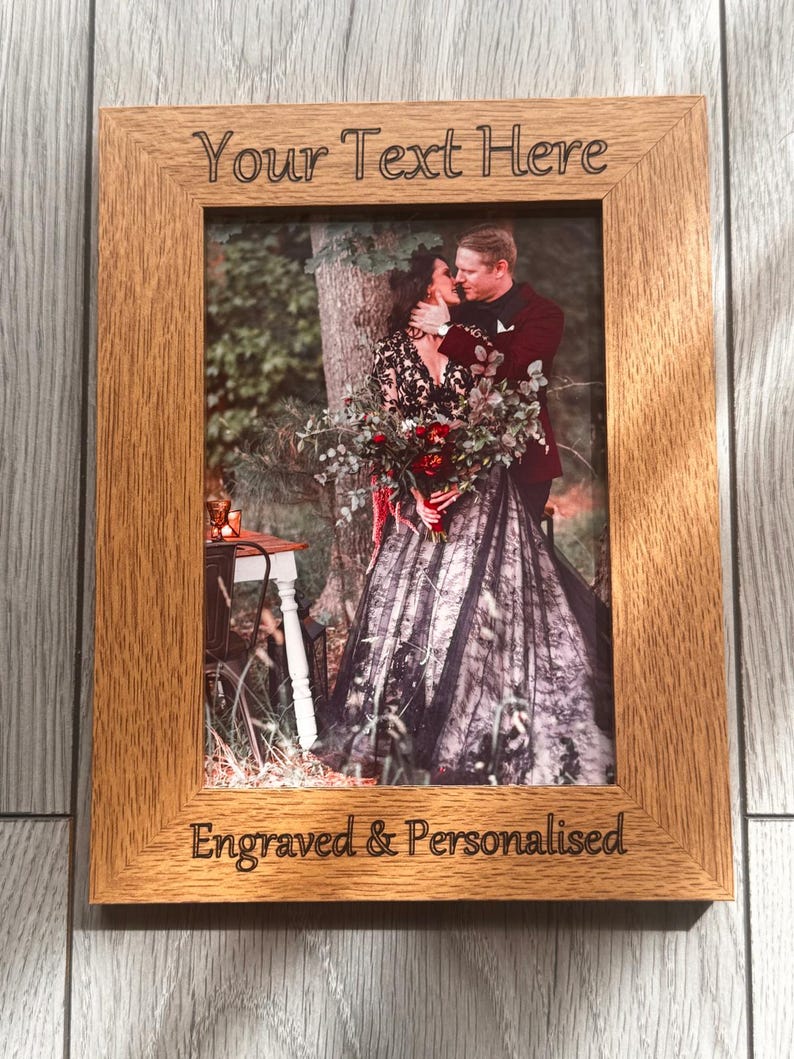 Op de afbeelding: Een rechthoekige houten fotolijst met de gegraveerde tekst "Your Text Here" en "Engraved & Personalised". De lijst bevat een foto van een knuffelend stel. De lijst is gemaakt van hout.
