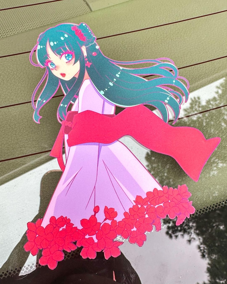 May include: A sticker featuring a cartoon anime girl with long teal hair wearing a pink dress and a red scarf. The girl is surrounded by pink flowers.