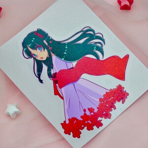 May include: A sticker featuring a cartoon illustration of a woman with long, dark green hair wearing a purple dress and a red scarf. She is surrounded by red flowers.
